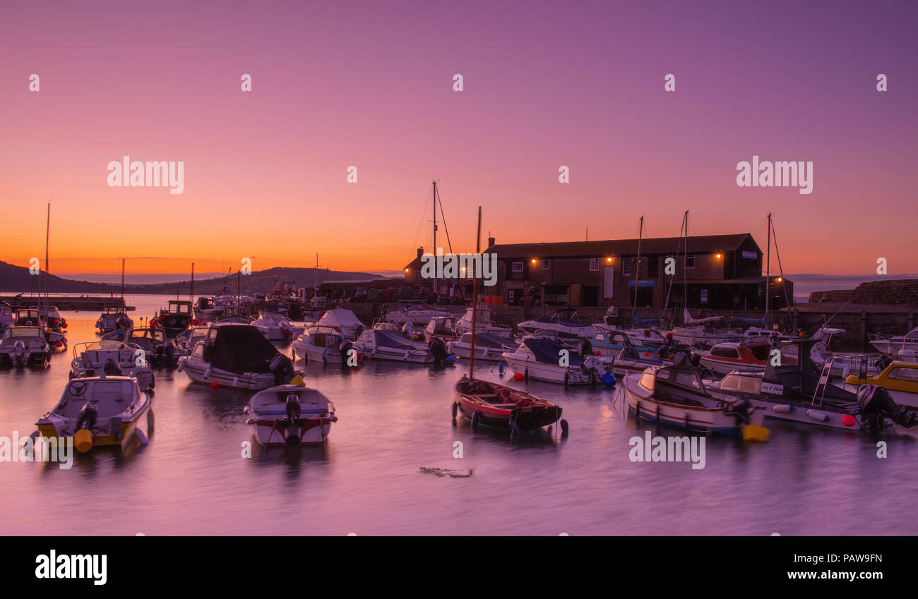 Lyme Regis, Dorset, Regno Unito. Il 25 luglio 2018. Meteo REGNO UNITO: Golden sunrise a Lyme Regis. Le barche nel porto si stagliano contro il bagliore dorato della mattina presto sky su un altro calda e soleggiata giornata nella località costiera comune di Lyme Regis. Credito: Celia McMahon/Alamy Live News. Foto Stock