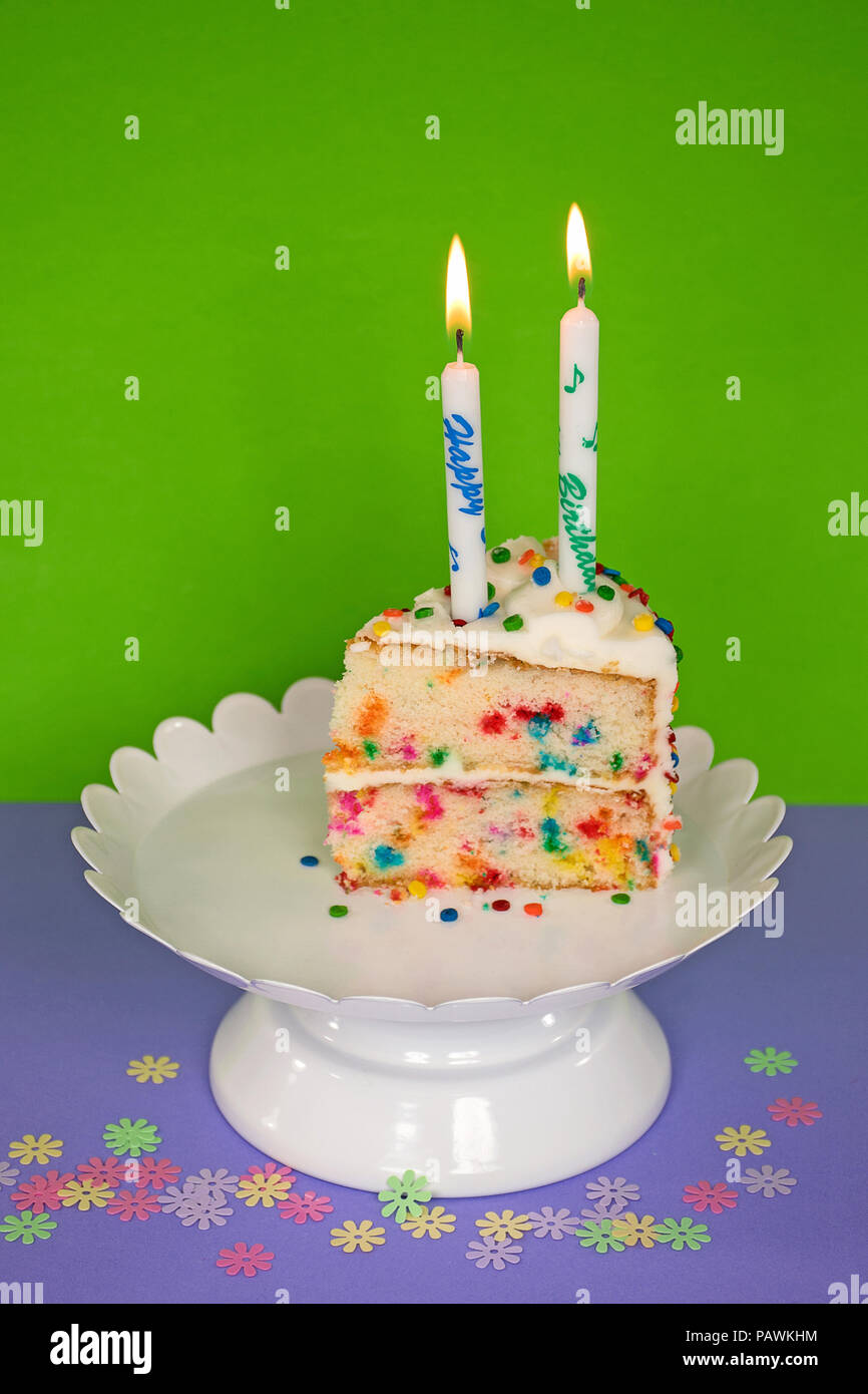 Fetta di torta di compleanno con candela sul piedistallo bianco piastra e coriandoli Foto Stock