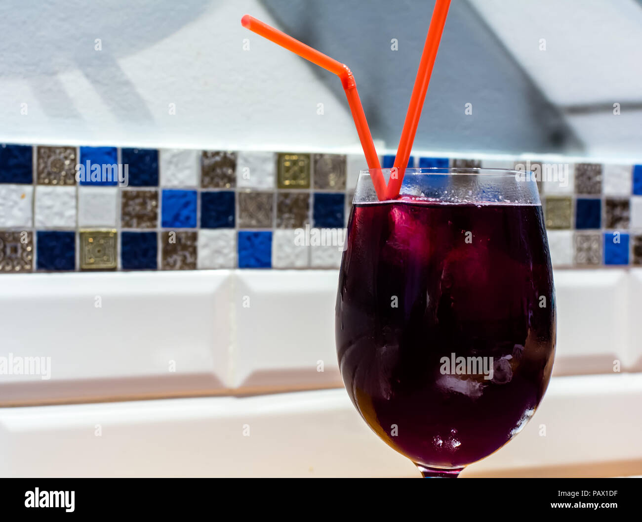 Bicchiere pieno di profondo rosso Sangria vino con due cannucce rosso sul bianco Sfondo piastrelle. La sangria è una bevanda alcolica di origine spagnola. Foto Stock