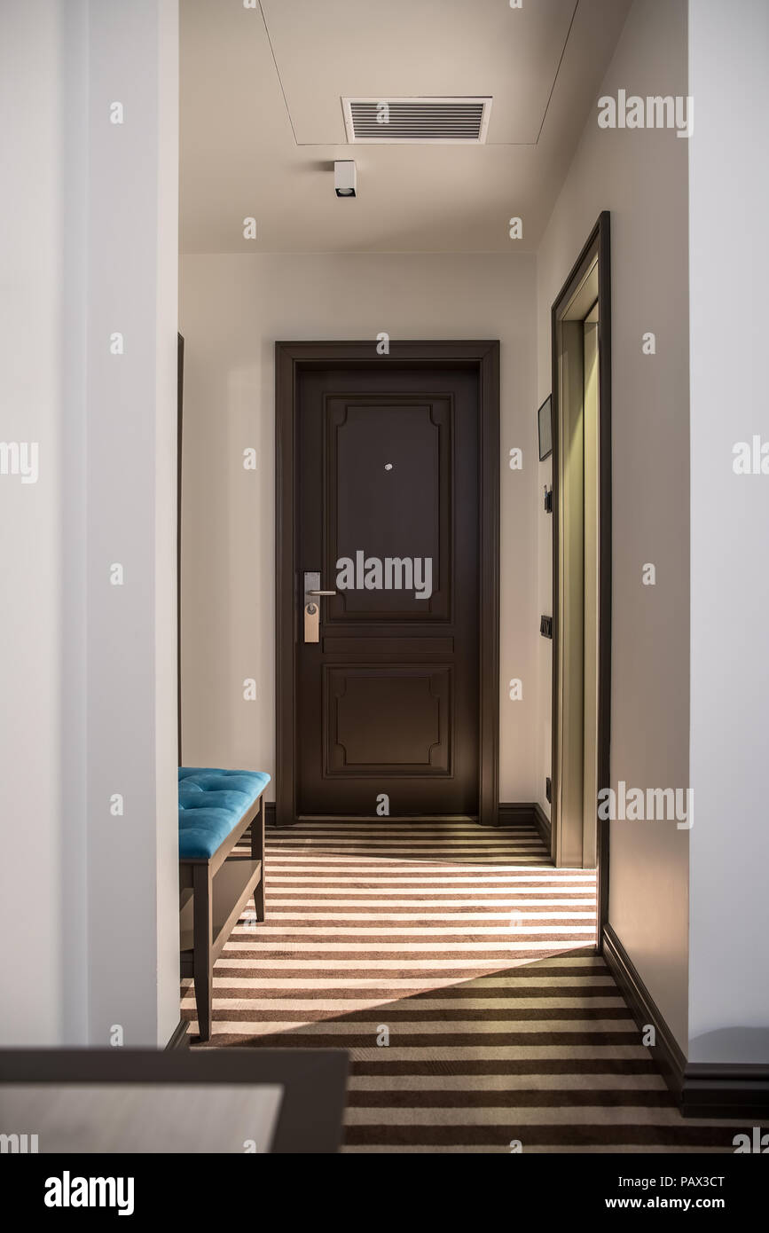 Corridoio illuminato in una stanza di un hotel con la luce pareti e un pavimento striato. Vi è un marrone porta di ingresso, un tavolo e un cavalletto di blu. Verticale. Foto Stock