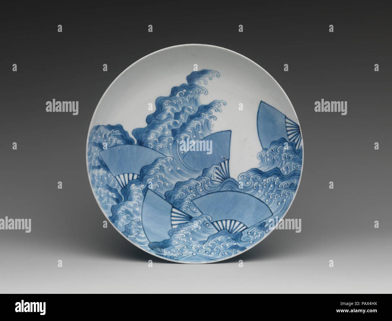 Piatto con ventole galleggiante su un flusso. Cultura: il Giappone. Dimensioni: H. 2 1/8 in. (5.4 cm); Diam. 7 7/8 in. (20 cm). Data: ca. 1730-1760s. Sebbene vari patterns in underglaze blu cobalto è apparso sulla parte esterna della proto-e inizio Nabeshima mercanzia, il classico modello che compare su molti dei pezzi da 1680s in poi è il contante e schema a pettine visto qui. Il contante è legato con nastro e compare sul bordo esterno del pezzo; il modello combinato viene visualizzato intorno alla parte esterna del poggiapiedi ad anello. Museo: Metropolitan Museum of Art di New York, Stati Uniti d'America. Foto Stock