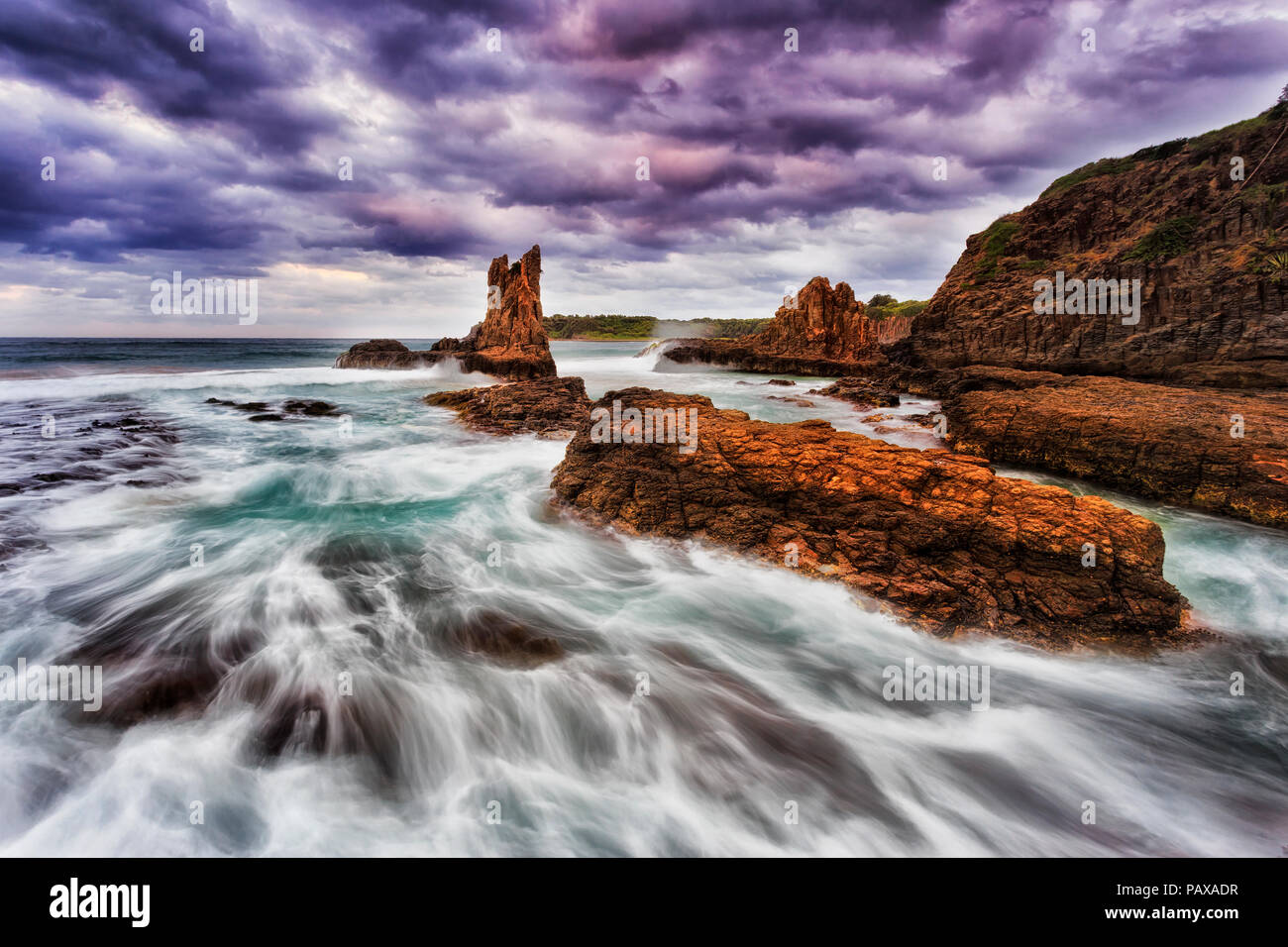 Colorato di dorata pietra arenaria cathedral rocks al Bombo beach in Kiama, NSW, Australia, al tramonto tempestoso sotto il cielo nuvoloso. Foto Stock