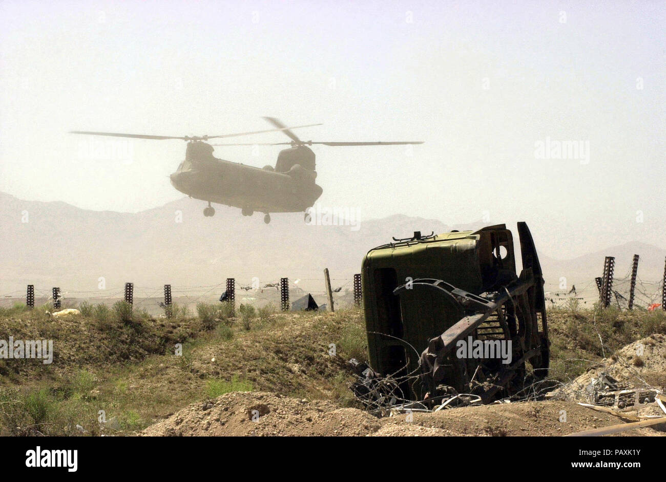 Un esercito americano (USA) CH-47 elicottero Chinook terre in condizioni polverose vicino al relitto di un veicolo abbandonato a Bagram Air Base. Un esercito americano (USA) CH-47 elicottero Chinook terre in condizioni polverose vicino al relitto di un veicolo abbandonato a Bagram Air Base (AB), in Afghanistan, durante l Operazione Enduring FREEODM. . Insieme con le dure condizioni molto di Bagram Air Base rimane riempita con promemoria dei passati conflitti militari come questo vecchio pezzo di militare sovietico hardware in primo piano. Foto Stock