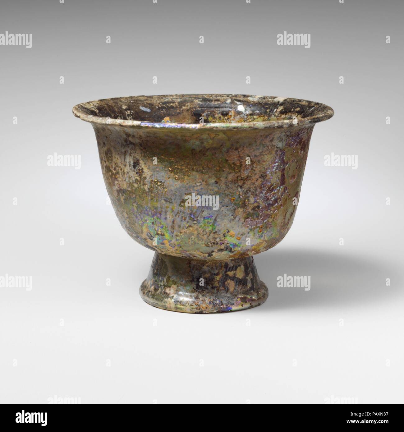 Vetro footed bowl. Cultura: Romano. Dimensioni: 3 1/8 in. (8 cm) di diametro: 4 1/16 x 4 3/16 x 2 1/8 in. (10.3 x 10.6 x 5.4 cm). Data: 3a-4a secolo D.C.. Traslucido blu pallido verde. Outsplayed, bordo arrotondato; lati convessi rastremantesi procedendo verso il basso, quindi ruotato a fondo piatto con cicatrice pontil; aggiunta di base ad anello con la svasatura di lati e spessa, bordo arrotondato. Intatti; pinprick bolle; fortemente alterate e snocciolate, con patch di brillanti iridescenza e smalto nero-come agenti atmosferici. Museo: Metropolitan Museum of Art di New York, Stati Uniti d'America. Foto Stock