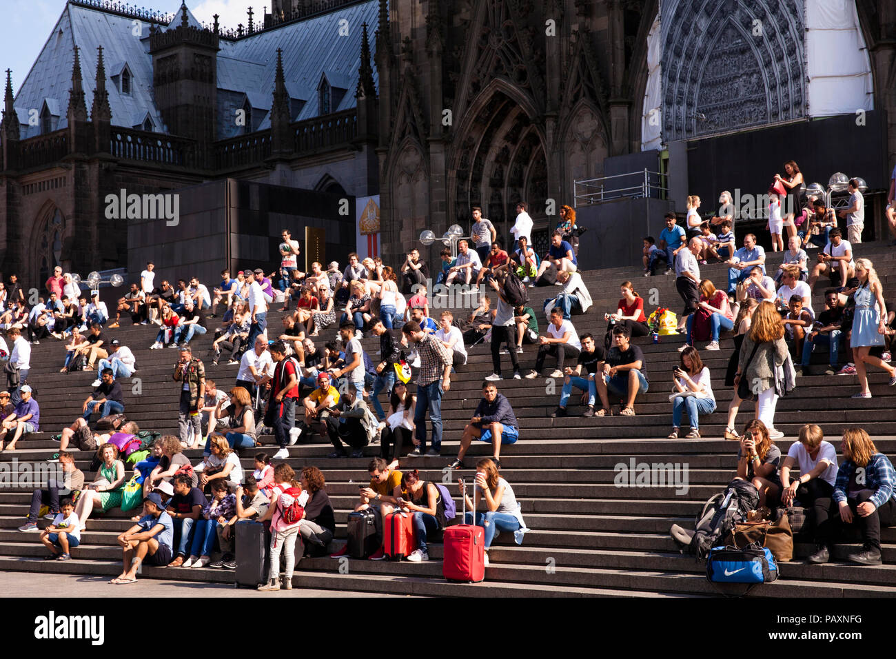 La gente seduta sulle scale formano la piazza del Duomo per la stazione principale di Colonia, Germania. Menschen sitzen auf der Treppe von der Domplatte zum ha Foto Stock