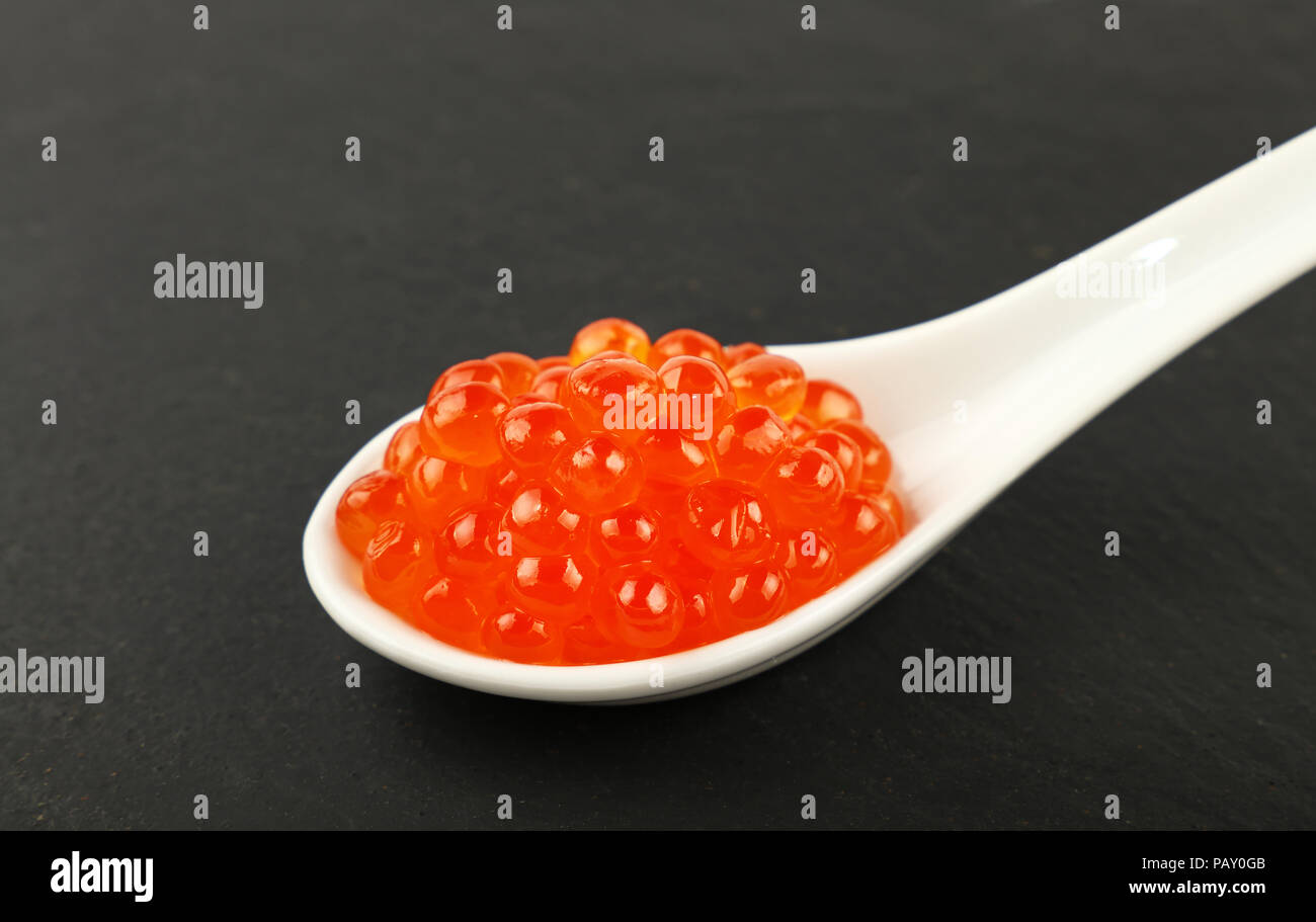 In prossimità di una porzione di pesce Salmone caviale rosso in cucchiaio bianco su sfondo di ardesia nera scheda cucina, ad alto angolo di visione Foto Stock