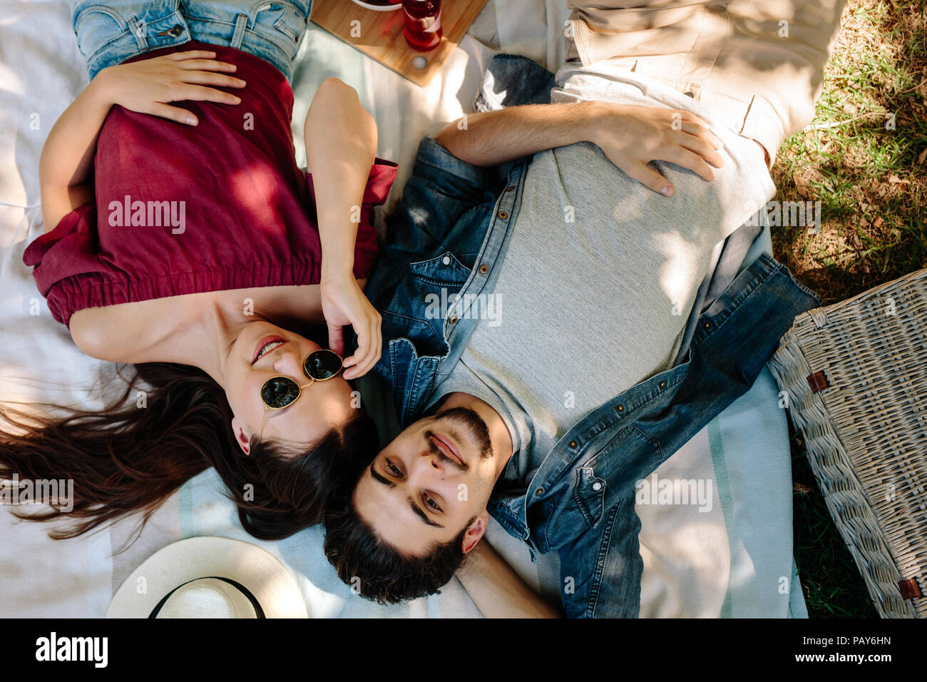 Girato dal di sopra della coppia giovane in amore giacente sulla coperta picnic. Uomo caucasico con la barba e la donna che indossa gli occhiali da sole rilassandosi insieme al parco. Foto Stock