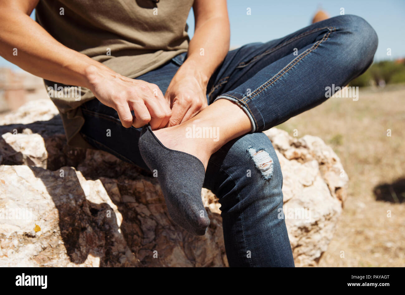 Primo piano di un giovane uomo caucasico seduto su una roccia all'aperto di mettere o togliere un Una low cut sock Foto Stock