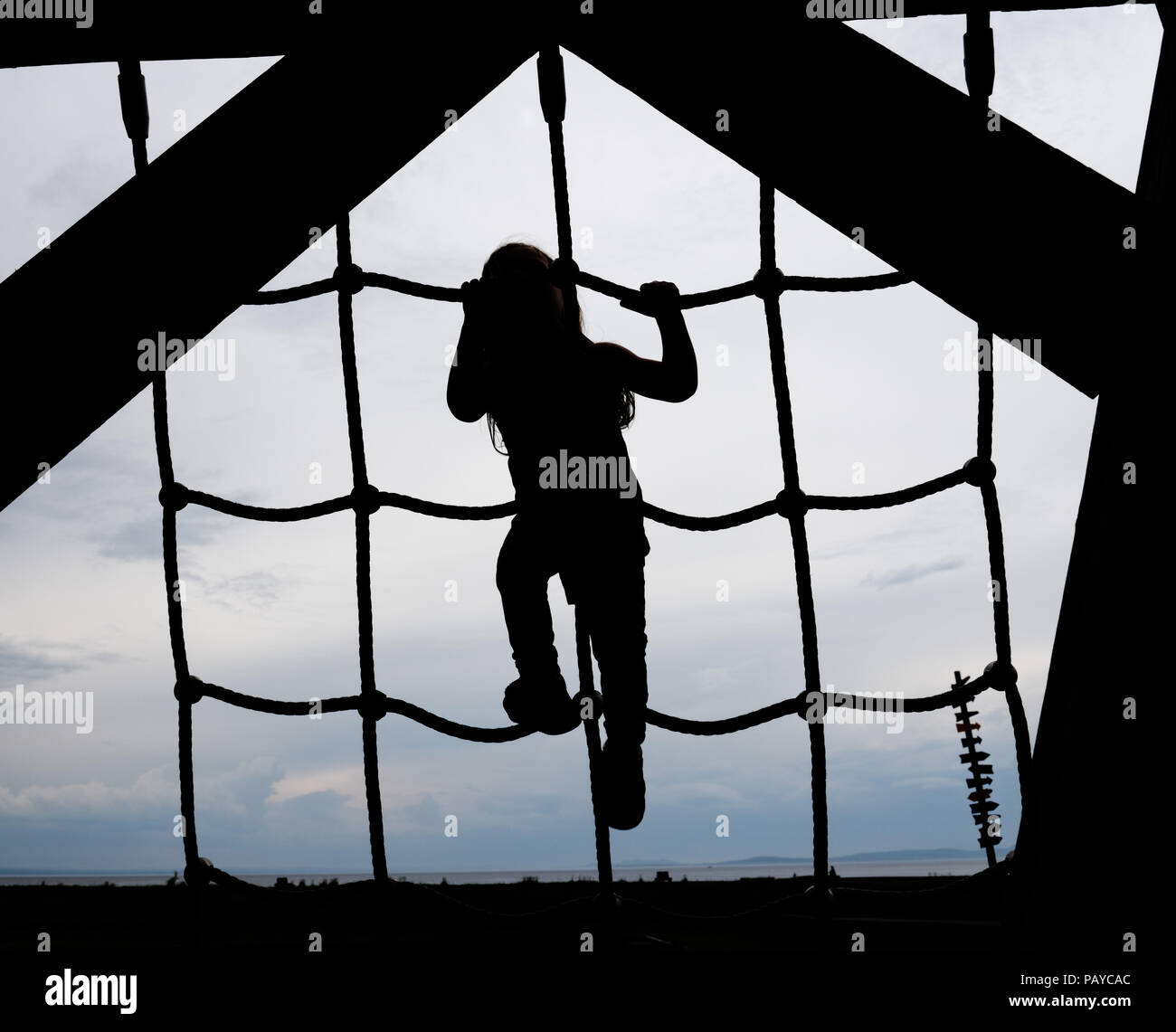 La silhouette di una bambina di tre anni la scalata di una scaletta di corda Foto Stock