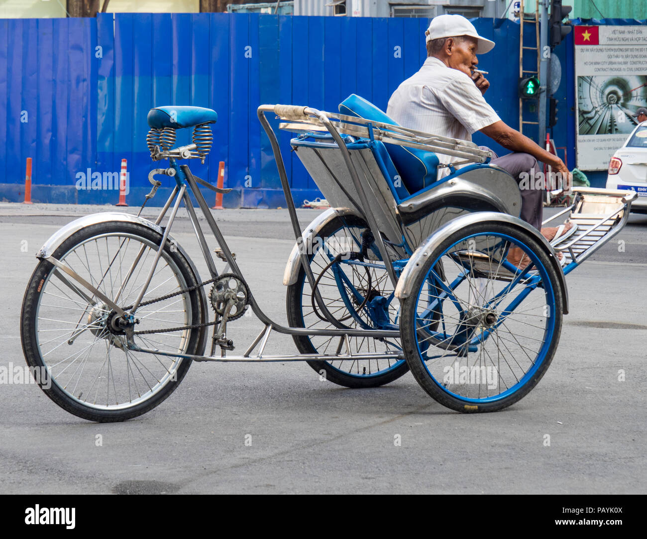 Anziani il vietnamita uomo seduto su un triciclo o risciò e fumare una sigaretta nella città di Ho Chi Minh, Vietnam. Foto Stock