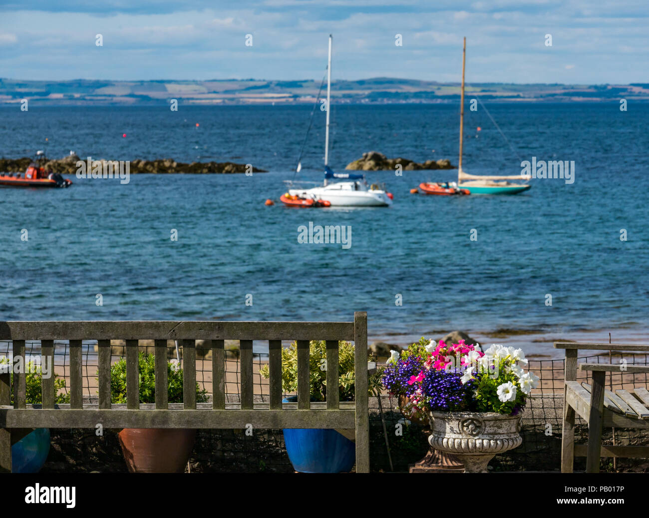 Fiori colorati e panche da casa al mare, West Bay Beach con ormeggiate barche a vela nel Golfo, North Berwick, East Lothian, Scozia, Regno Unito Foto Stock
