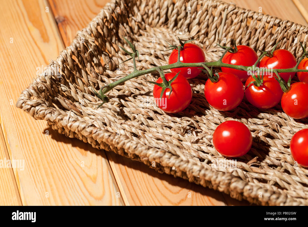 Red Cherry vine maturate al sole piccolo pomodori nel cesto di vimini vassoio. Dolci sani organico rosso pomodoro in miniatura dello stelo. Foto Stock