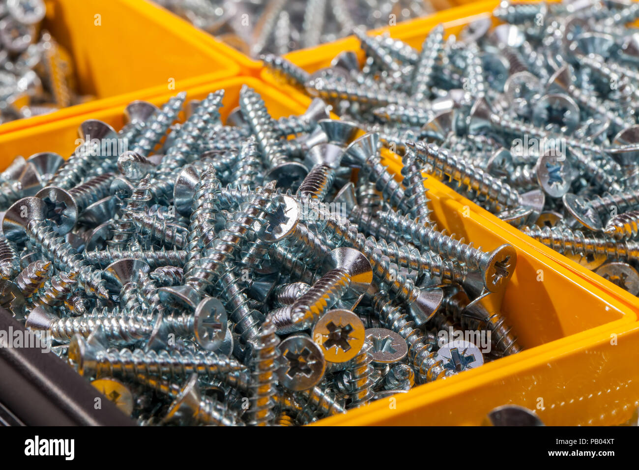 Woodscrews. Pila di testa a croce viti per legno ordinati nella casella gialla contenitore di storage. Assortimento di argento woodscrews DIY in stretta verso l'alto. Foto Stock
