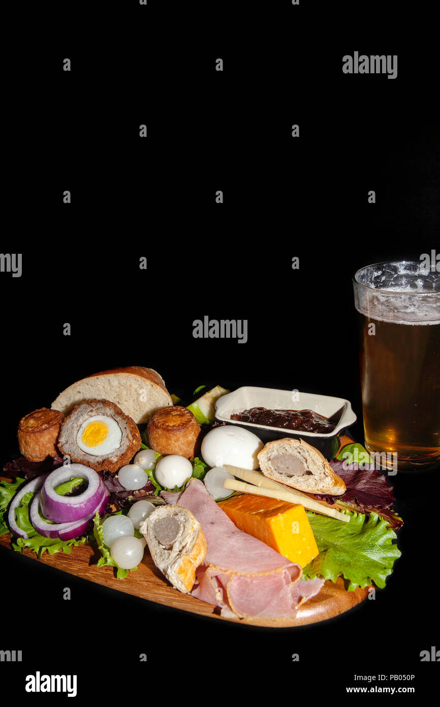 Pub inglese tradizionale pasto di un plowman pranzo servito con una pinta di birra lager. Il tipico cibo freddo include pasticci di carne di maiale e prosciutto, uova sode e c Foto Stock