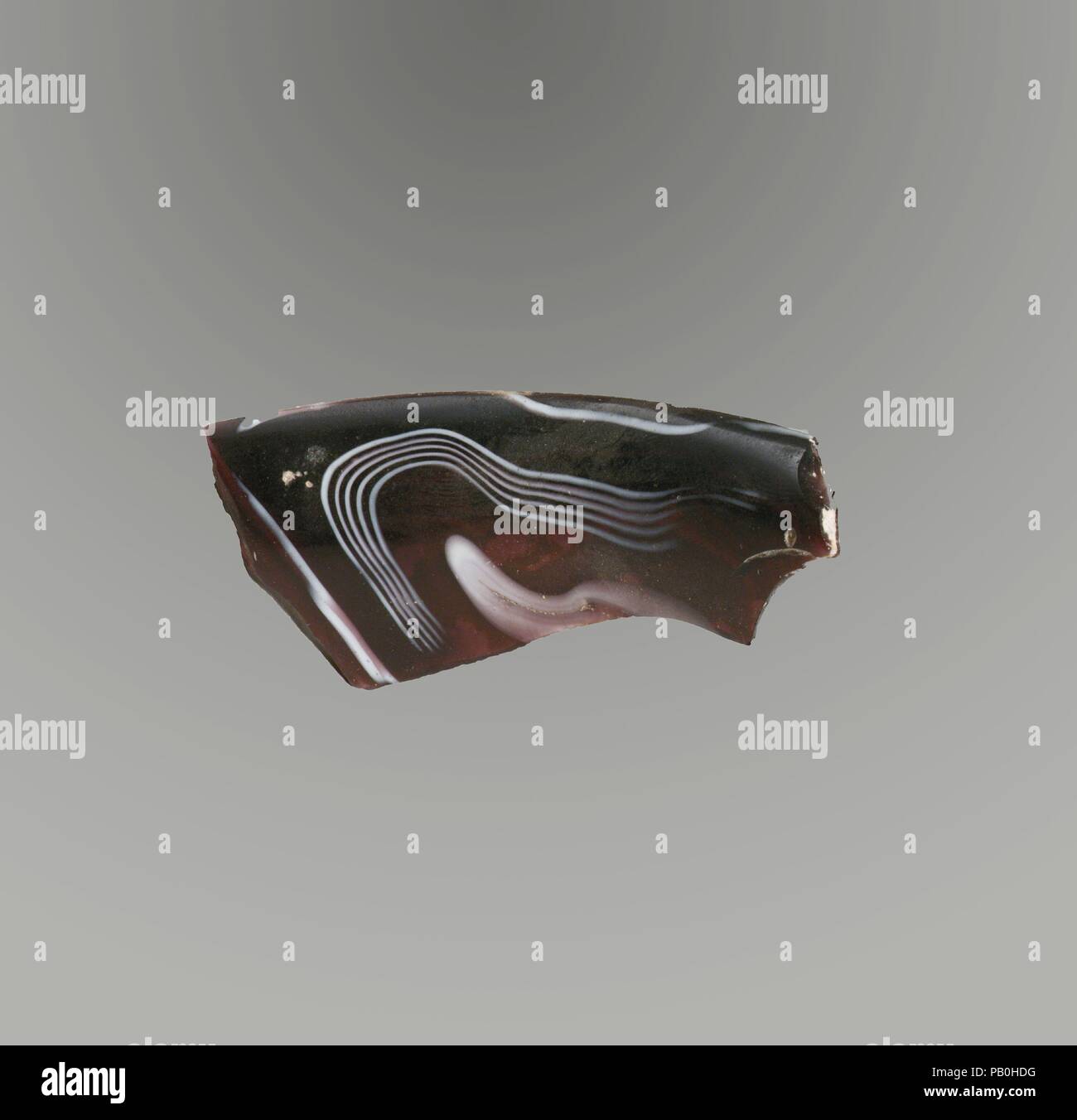 Mosaico di vetro scanalata frammento di ciotola. Cultura: Romano. Dimensioni: Altri: 1 3/8 x 2 3/4 in. (3,4 x 7 cm); stima diam. del cerchio 7 5/8 in. (19,4 cm). Data: fine del I secolo A.C. - inizio del I secolo d.c. Traslucidi viola e bianco opaco. Spesso, quasi cerchio orizzontale con bordo arrotondato; lato dritto leggermente rastremata verso il basso. Spirale in mosaico formata da spezzoni di una o più canne in una massa di colore viola con spirali di bianco e filettature fini in linee parallele; sulla parte esterna, tracce di uno verticale nervatura poco profonde. Lucidati interno; vaiolatura di bolle di superficie; opacizzazione, cremosa, resistenza agli agenti atmosferici e così Foto Stock