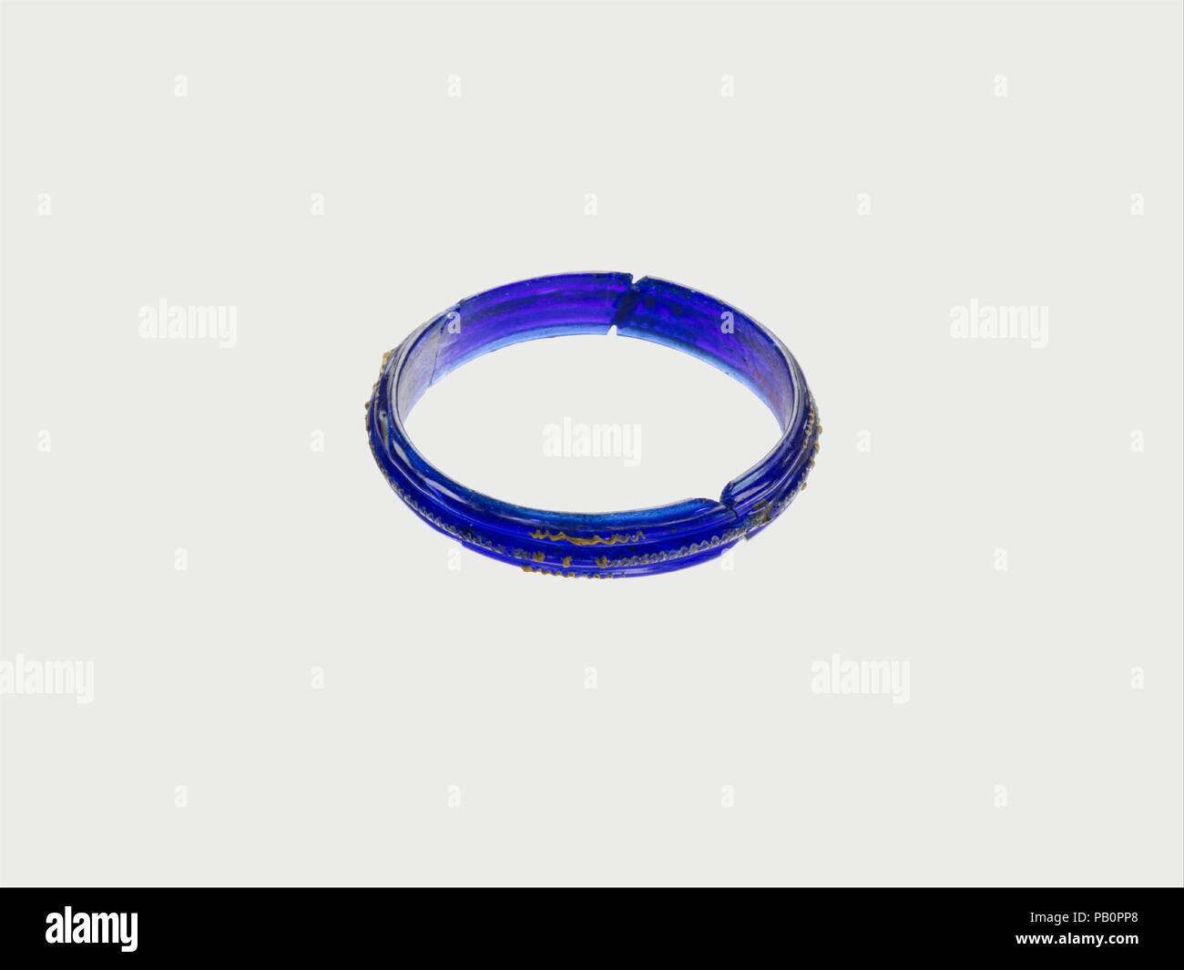 Bracciale in vetro. Cultura: Celtic. Dimensioni: 9/16a. (1.4Cm) altri: 3 3/16a. (8.1Cm). Data: fine 3rd-2nd secolo A.C. Traslucido blu cobalto; percorsi in opaco giallo. Seamless a larga banda appiattita con sezione trasversale semicircolare. Sulla superficie esterna, tre nervature che corre intorno a banda, uno centrale sporgente fuori più; nervature esterne decorate con quattro lunghezze corrispondenti del sentiero a zig-zag; costola centrale con quattro lunghezze di percorso a zig-zag intervallati con quattro gruppi di tre blob. Rotto e riparato con chip mancante da bordi rotti e alcuni dei sentieri mancante, lasciando incavi nella superficie di Foto Stock