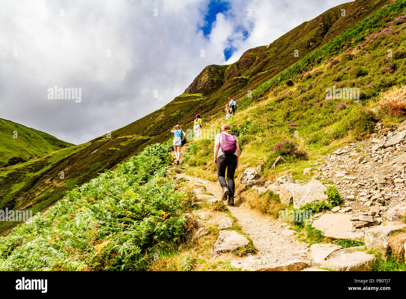 Gli escursionisti in abiti estivi camminando su di una ripida via a Loch Skeen dal grigio mare di coda della Riserva Naturale a Moffat colline. La Scozia, Regno Unito. Foto Stock