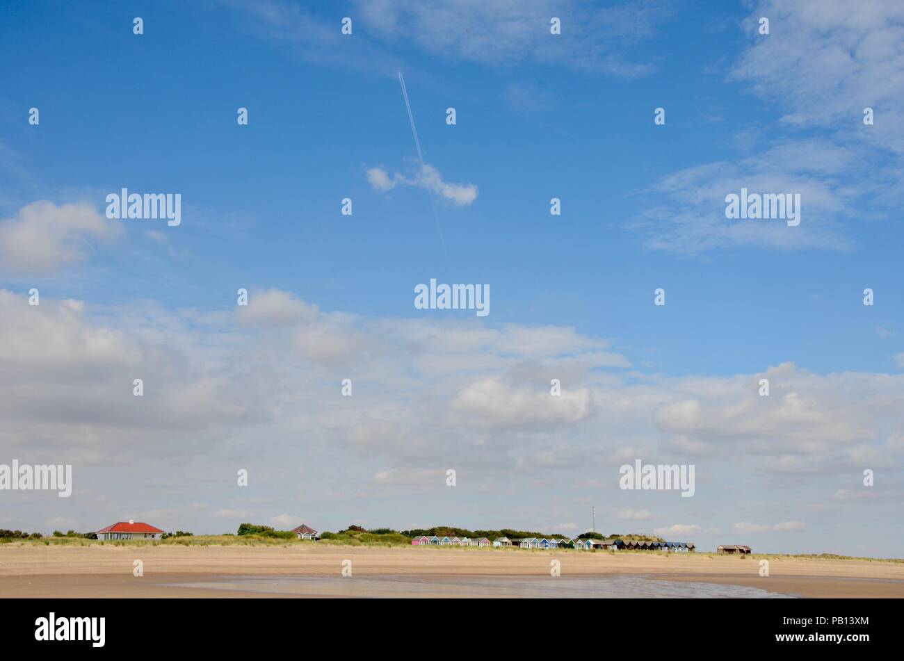 Big Blue sky con aeromobili sentiero di vapore al di sopra di mare chalets in dune di sabbia, Lincolnshire coast, Inghilterra, Regno Unito. Foto Stock