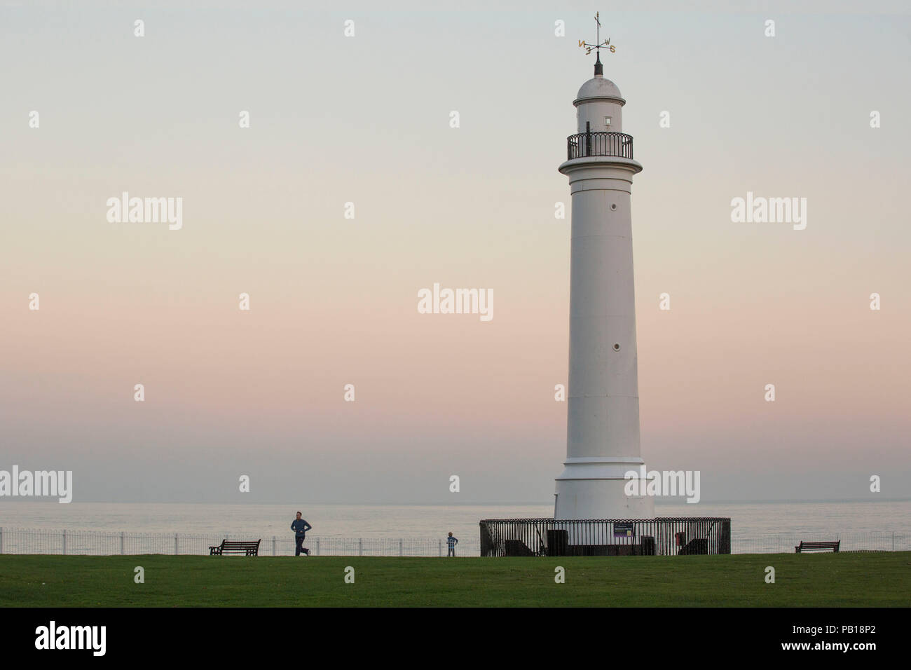 Jogging sul lungomare con il faro in Shot, Costa Nord Est. Regno Unito Foto Stock