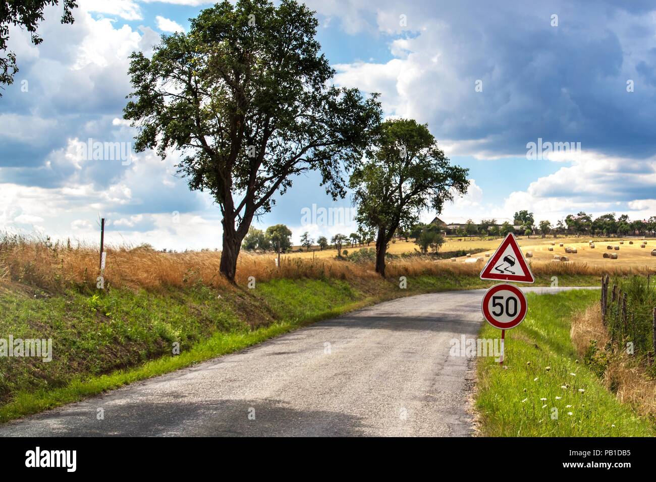 Strada segno di avvertimento sul fondo stradale sdrucciolevole. Eventuali fuoriuscite di ghiaia sulla strada. Giorno di estate sulla strada. Giornata calda. Foto Stock