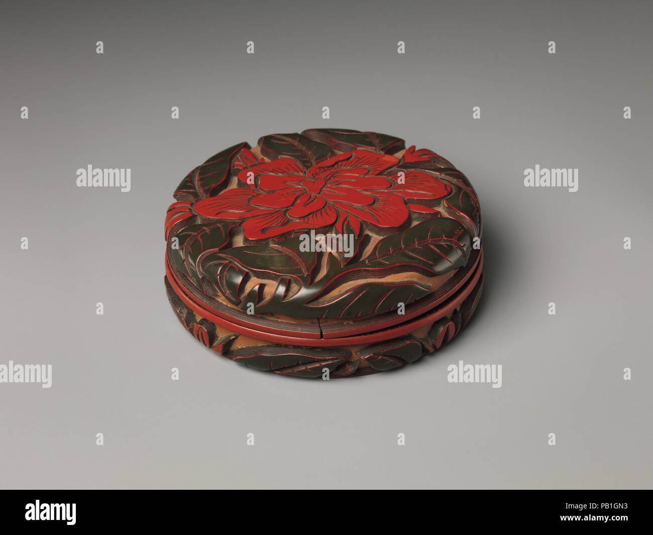 Scatola con camellia. Cultura: la Cina. Dimensioni: H. 1 3/8 in. (3,5 cm); Diam. 4 a. (10,2 cm). Data: XIV secolo. I fiori stilizzati raffigurato in lacca della Cina sono spesso difficili da identificare con precisione. Tuttavia, il grande fiore su questa casella è probabilmente una camelia, un fiore associato con l'inverno e endurance. Questa casella è uno dei vari, la maggior parte ha trovato in Giappone, che portano il nome di Zhang Cheng (qui, intagliato nella base). Egli è uno dei due soli trecento artisti di lacca i cui nomi sono registrati. Museo: Metropolitan Museum of Art di New York, Stati Uniti d'America. Foto Stock