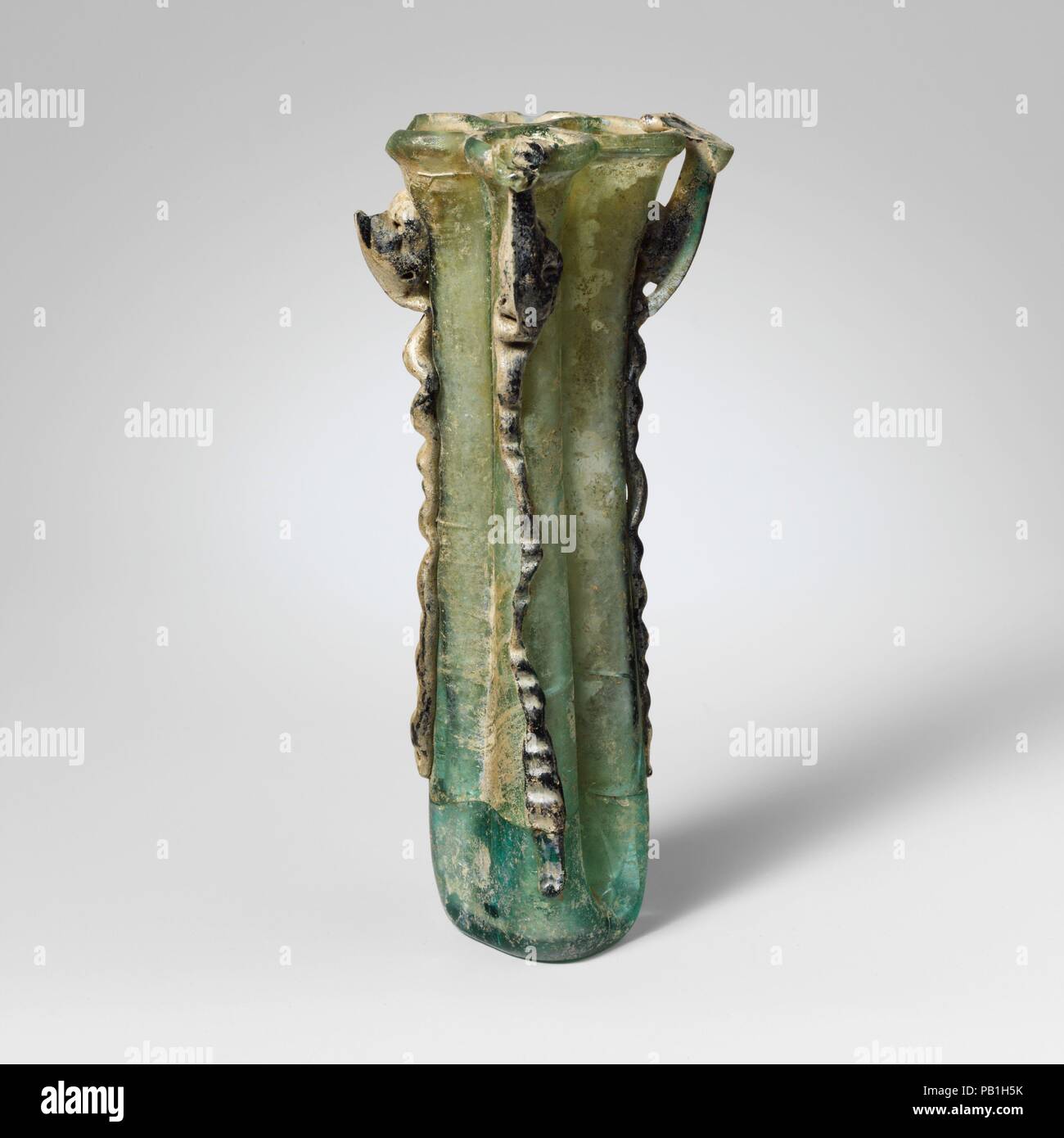 Vetro pallone cosmetici con quattro scomparti (kohl tubo). Cultura: romana, Palestina. Dimensioni: complessivo: 6 1/2a. (16,5 cm). Data: 4th-5secolo D.C.. Blu traslucido verde; gestisce e sentieri in parte nello stesso colore, parzialmente nel profondo blu traslucido, appaia nera. Rovesciato cerchio tubolare, ripiegato su se stesso e in; corpo comprendente quattro tubi affiancati in una ruvida forma quadrata, realizzato a partire da un unico gonfiato raccogliere mediante pinzatura e piegatura a lati verticalmente per rendere il diaframma; a fondo piatto con cicatrice pontil; quattro maniglie, applicato sulla sommità dei percorsi verticali, redatto e fuori, e verso il basso, quindi rivolta verso l'interno Foto Stock