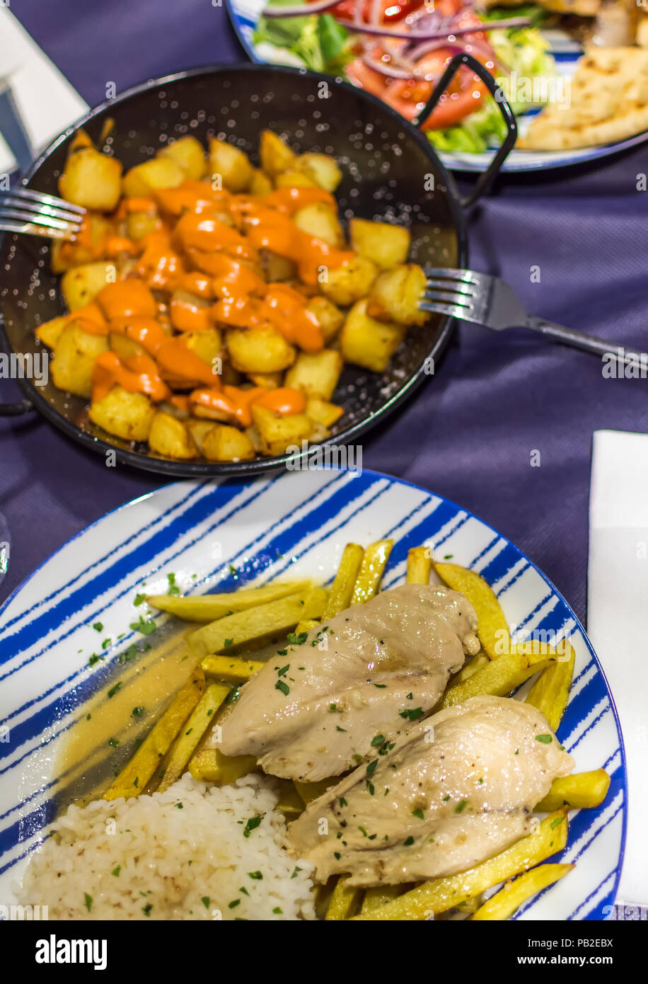 Pollo al limone con patatine fritte fatte in casa, patatas bianche (spagnolo patate fritte) e pollo gyros con chip fatti in casa e insalata di verdure. Foto Stock