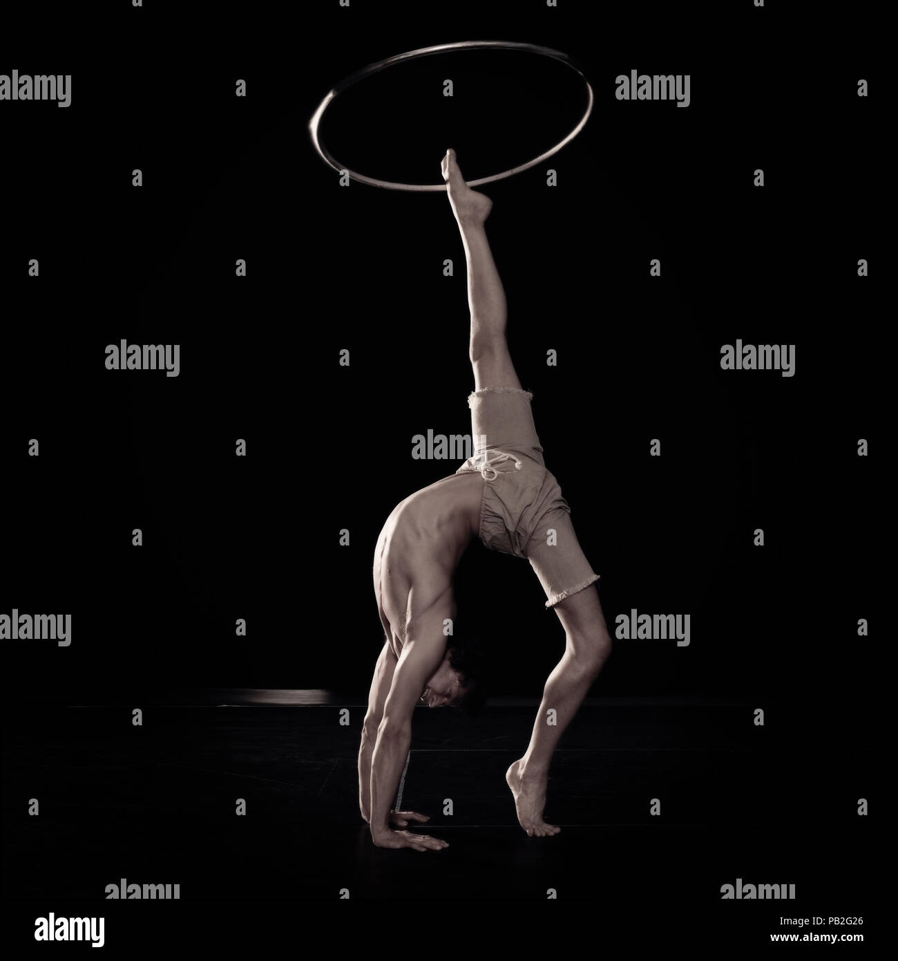Un circense facendo una schiena curva e gruppi con un hula hoop fa roteare fuori un piede. Foto Stock