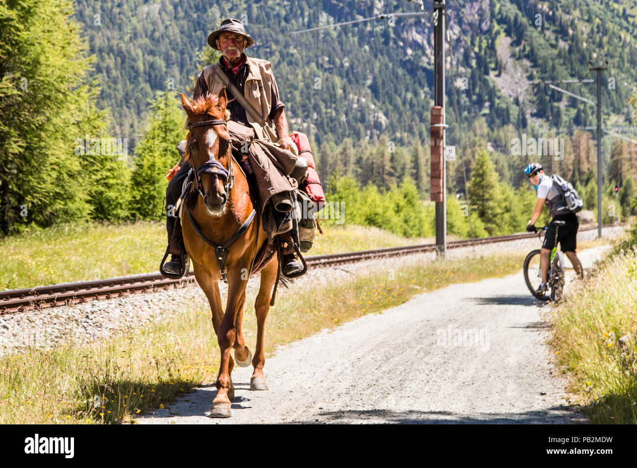 Escursione a cavallo a Graubünden, Svizzera. Il direttore dell'hotel sulla e-bike è stupito. Anche lui non vede un viaggiatore che attraversa i Grigioni a cavallo ogni giorno. Foto Stock