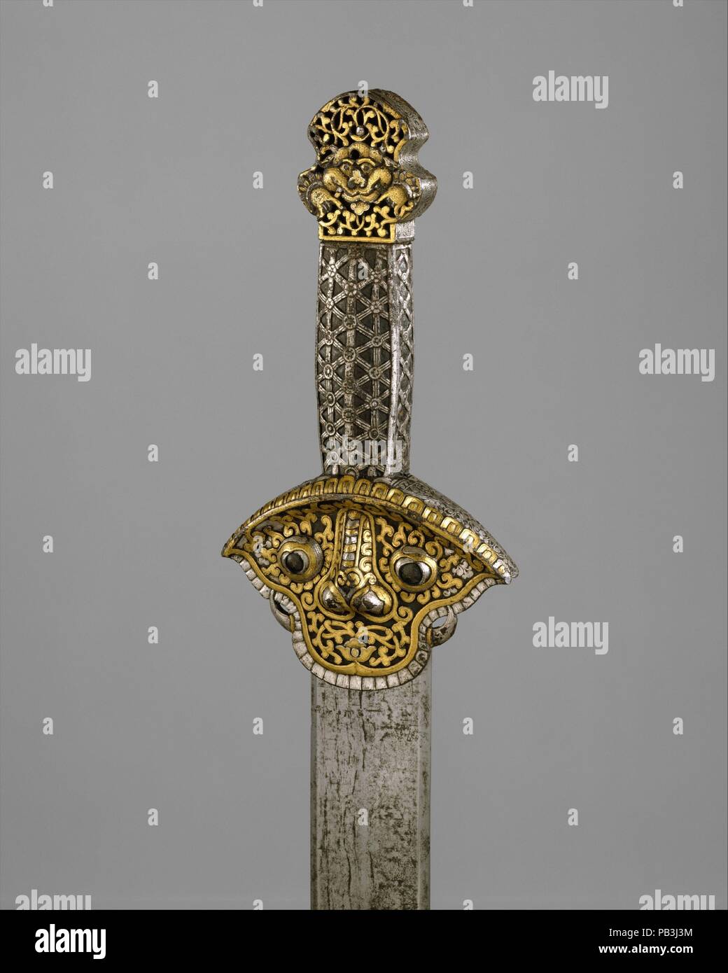Spada (Ral gri). Cultura: tibetano o cinese. Dimensioni: L. 34 7/8 in. (88,6 cm); L. della lama 29 1/2 in. (74,9 cm); W. 3 7/8 in. (9,8 cm); Wt. 2 lb. 2.5 oz. (978.1 g). Data: xiv secolo - XVI secolo. Questo è uno dei migliori esempi di un piccolo gruppo di prima rara spade dal Tibet. L'elsa di questa spada, compresa la sua impugnatura è realizzata interamente in ferro che è stato goffrato, cesellato e quindi damascened in oro e argento. La guardia, appena al di sotto della presa, è sotto forma di una maschera stilizzata con denti e zanne, che rappresenta una divinità protettiva o tutore di figura. Dritto a doppio taglio lame di questo Foto Stock