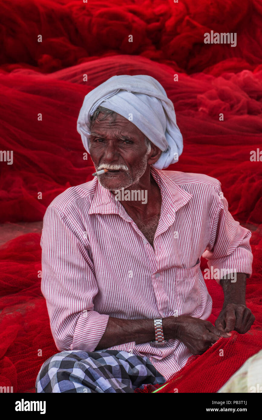 Un pescatore del Kerala mende uno dei rossi locali reti da pesca Foto Stock