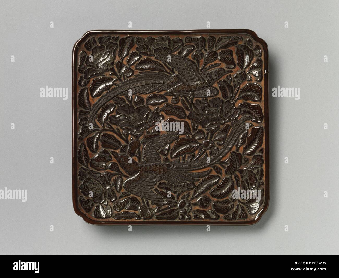 Piatto quadrato con una lunga coda di uccelli e camelie. Cultura: la Cina. Dimensioni: H. 1. (2,5 cm); W. 7. (17,8 cm); L. 7 1/8 in. (18 cm). Data: XIV secolo. Realizzato in un classico due-bird design, questo piatto è rappresentativo di stile dei primi anni del XIV secolo. L'artista lacca raggiunto quasi una immagine tridimensionale su una superficie piana: deep carving crea l'effetto di rilievo e di sottili incisioni per le piume di uccelli e di foglia vene convogliare texture. Lo sfondo rosso è relativamente visibile rispetto agli esempi fatti più tardi nel corso del secolo. Museo: Metropolitan Museum of Art di New York, Stati Uniti d'America. Foto Stock
