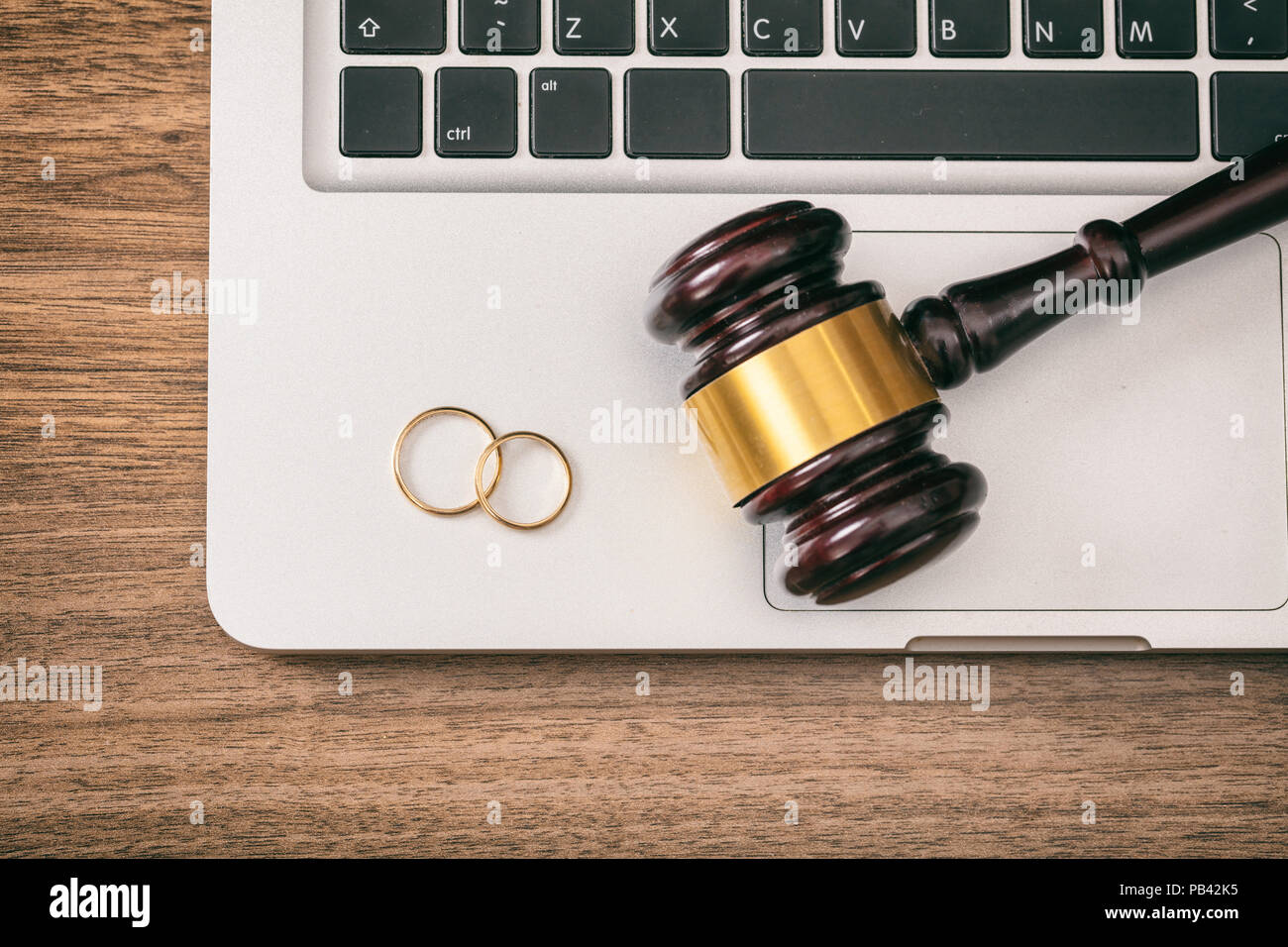 Concetto di divorzio. Gli anelli di nozze e giudice martello sul computer portatile, sullo sfondo di legno, vista dall'alto Foto Stock