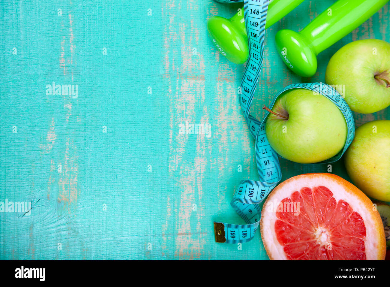 Cibo per la dieta e manubri su un verde sullo sfondo di legno. Concetto di dieta e stile di vita sano. Foto Stock