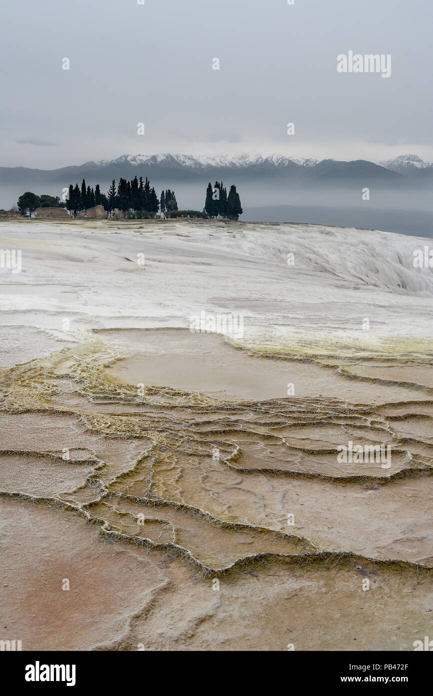 Una vista di fronte di Pamukkale terrazze di travertino di alcune rovine e un cluster di alberi con montagne innevate sullo sfondo. Pamukkale, Turchia. Foto Stock