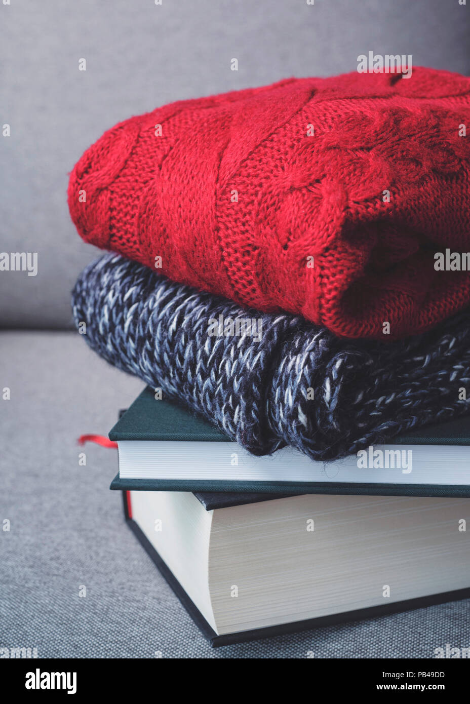 Hugge autunno inverno concetto, rosso maglioni e libri su sfondo grigio, freddo, casa accogliente Foto Stock