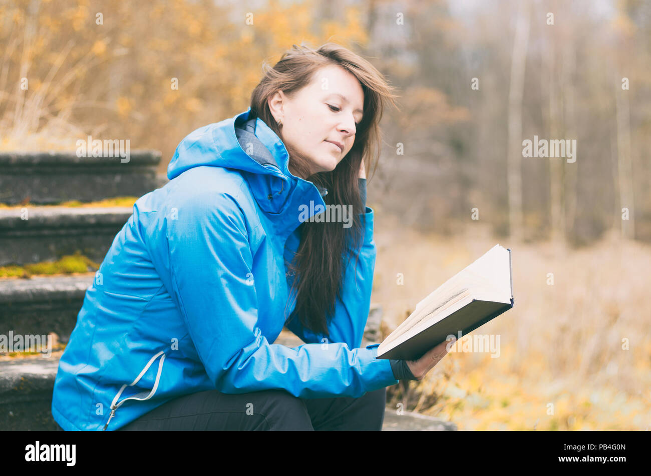 Autunno ragazza senza trucco con capelli disheveled premurosamente la lettura di un libro sullo sfondo di La natura in autunno. Film stilizzato. Foto Stock