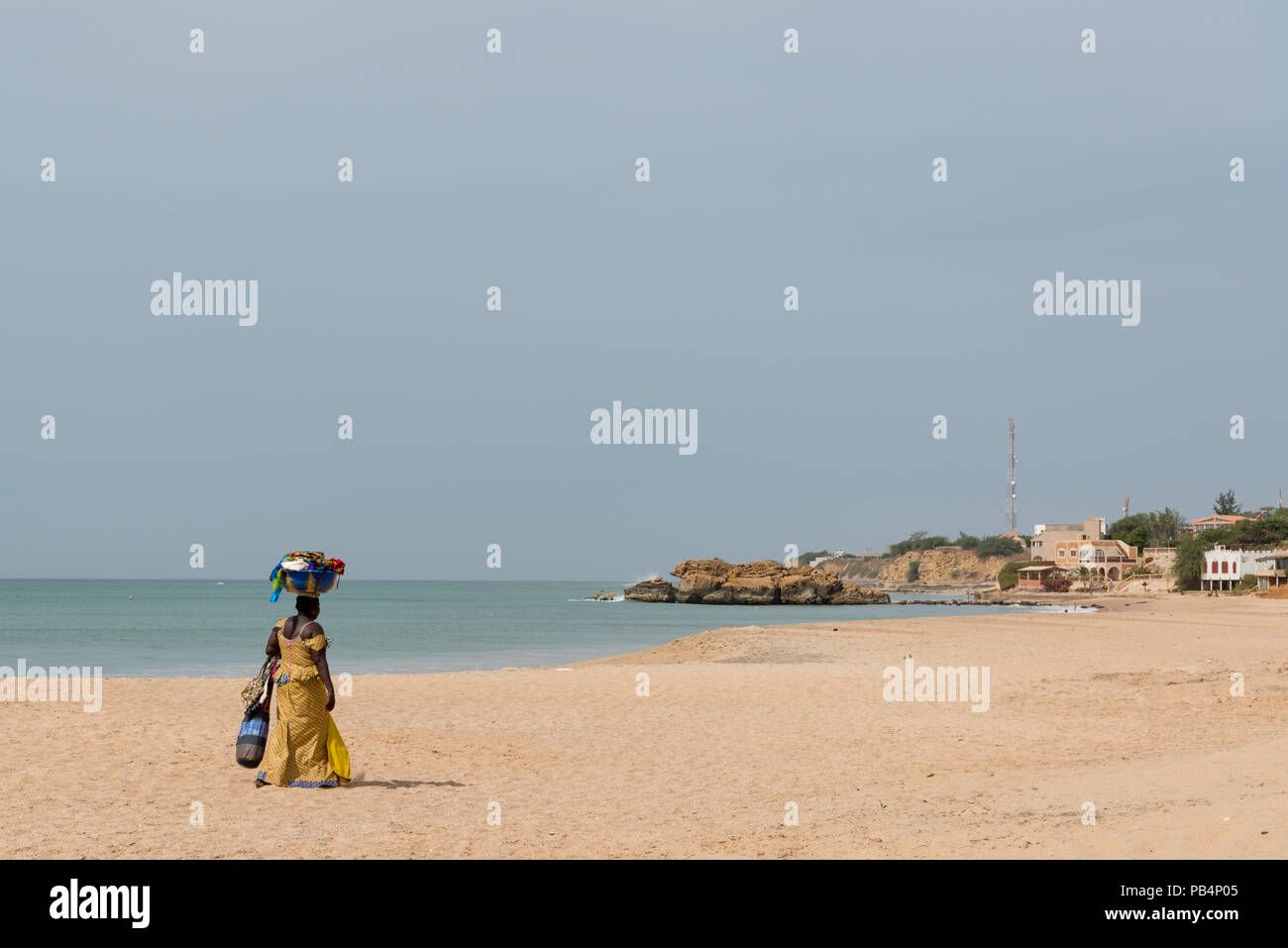 Una donna a piedi lungo la spiaggia di Popenguine con un cesto di merce da vendere sul suo capo, Thies, Senegal Africa occidentale Foto Stock