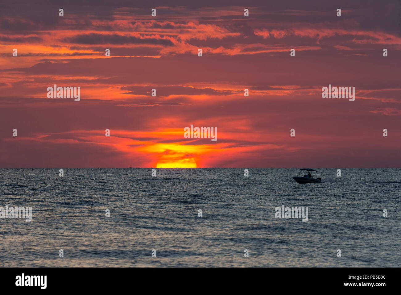 Piccola barca con il sole che tramonta parially dietro le nuvole in cielo arancione sull'acqua nel Golfo del Messico Foto Stock