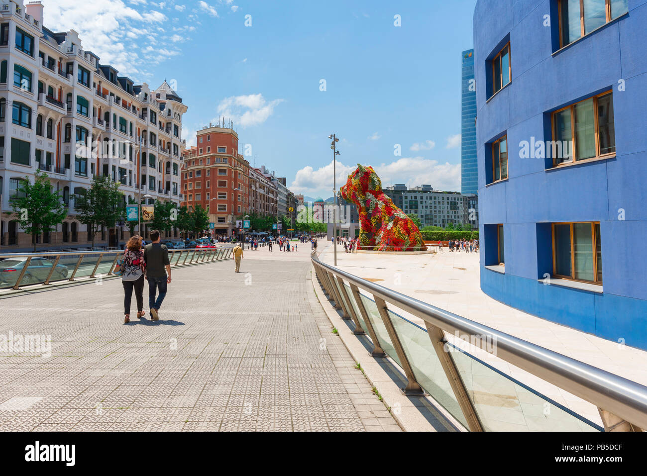 Bilbao city art, una giovane coppia a piedi verso il grande fiore cucciolo rivestito di Jeff Koons situati al di fuori del Museo Guggenheim a Bilbao, Spagna settentrionale. Foto Stock