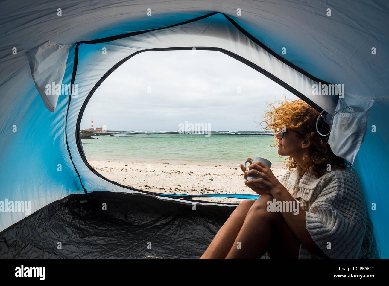 Lonely bella donna seduta sulla tenda guardando al di fuori del vento sui capelli e campeggio sulla spiaggia vicino i colori di acqua e terra. Libertà e Foto Stock