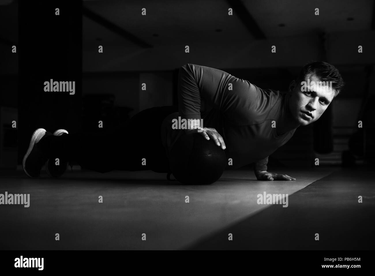 Bel giovane uomo che fa pushups con Palla medica come parte della formazione bodybuilding Foto Stock