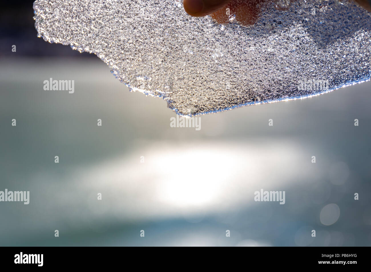 Mano che tiene un pezzo di ghiaccio rotto fino al sole Foto Stock