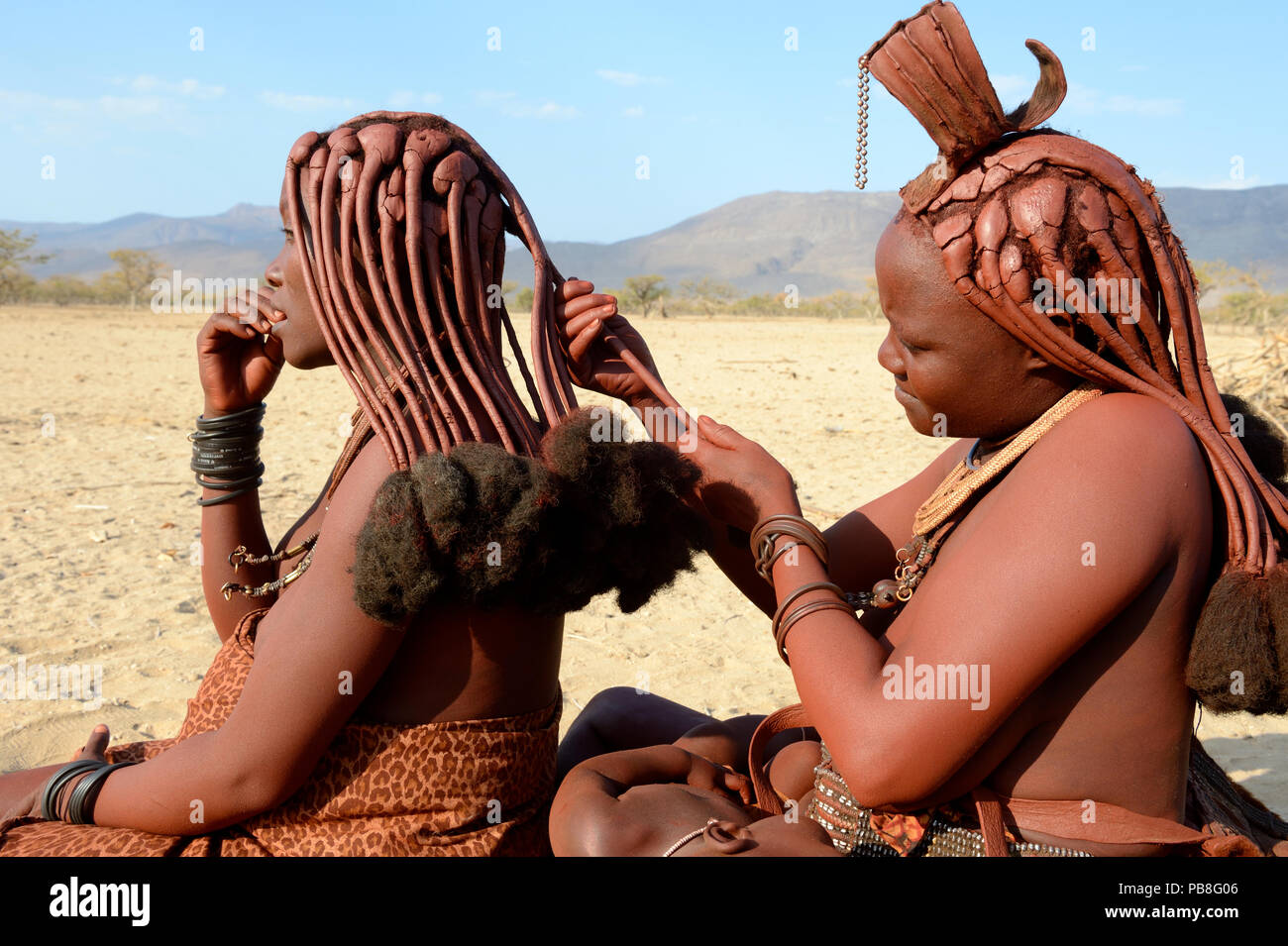 Le donne himba trecciatura reciprocamente i capelli. Marienfluss Valley. Kaokoland, Namibia Ottobre 2015 Foto Stock