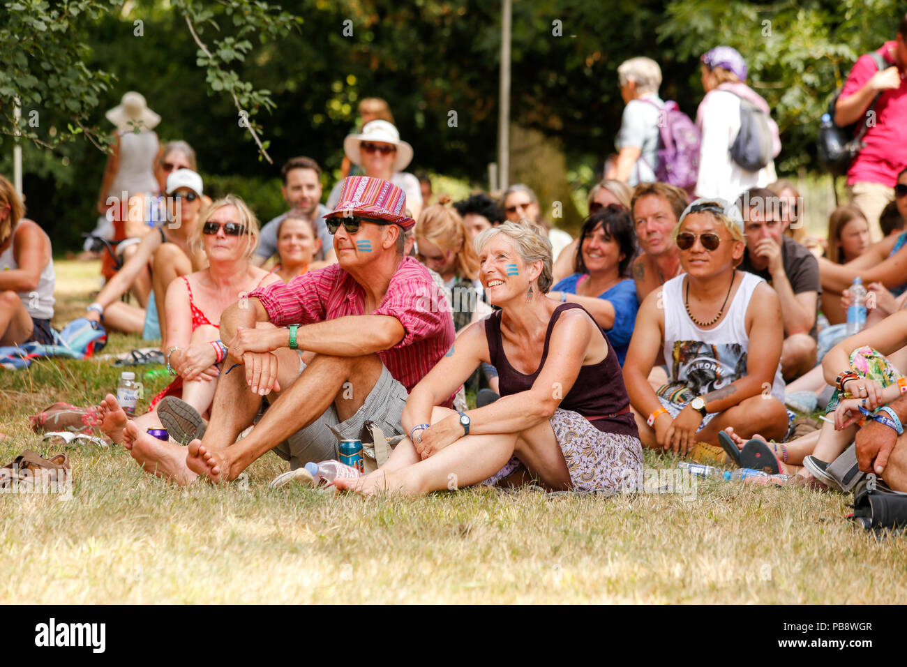 Charlton Park di Malmesbury, Wiltshire. Il 27 luglio 2018. Il festival prende il via in condizioni calde e umide per la sua prima giornata piena di musica del mondo, il teatro di strada e workshop. La folla prende ombra e godere di una parola detta sessione di poesia nell'arboreto. Credito: Wayne Farrell/Alamy Live News Foto Stock