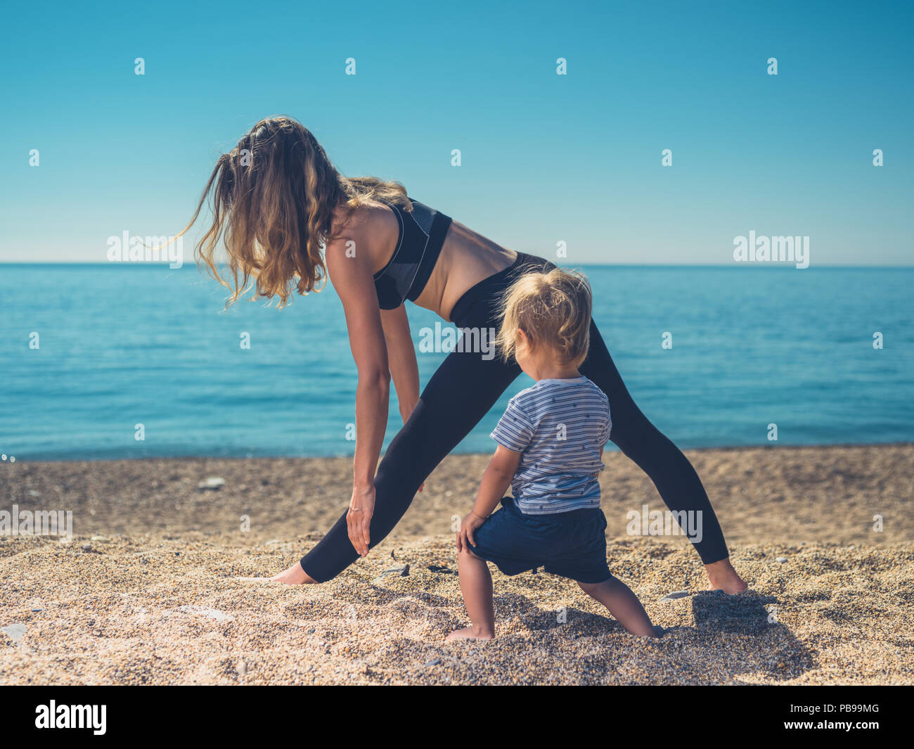Una giovane madre sta facendo yoga sulla spiaggia con il suo bambino Foto Stock