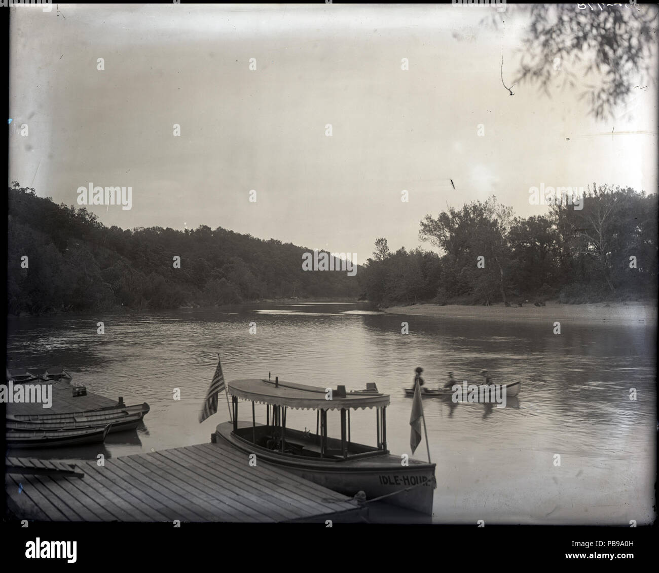 . Inglese: orizzontale, fotografia in bianco e nero che mostra un battello chiamato 'Inattiva Hour' legato a un dock in primo piano. Dietro "Idle Hour', due uomini e una donna sono in barca in una piccola barca a remi. Linea di alberi le rive del fiume e il fiume curve a destra sullo sfondo. Titolo: le barche da diporto su un fiume. Tra il 1910 e 1920 1249 Le barche da diporto sulle rive di un fiume Foto Stock