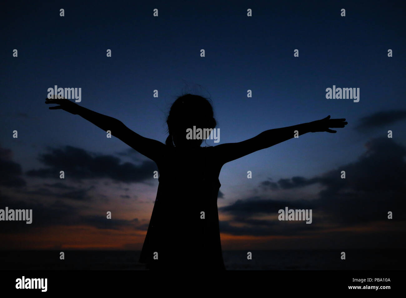 Silhouette della bambina con le mani tese nel Cielo di tramonto sullo sfondo. Foto Stock