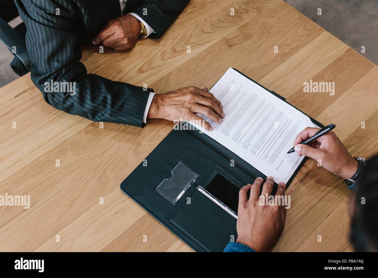 Vista dall'alto di due uomini di affari firma contratto le carte sul tavolo. Mani di business executive la firma dei documenti in ufficio. Foto Stock