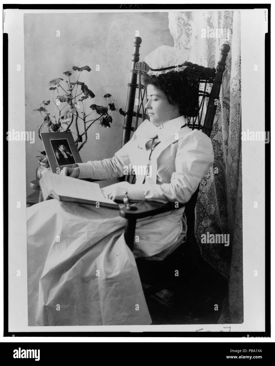 1122 studente infermieristica indossando un starched bianco uniforme, seduto in una sedia a dondolo, lettura LCCN99472219 Foto Stock